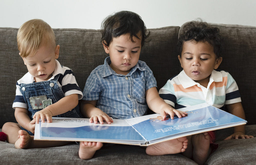 Three kids reading a book on the sofa