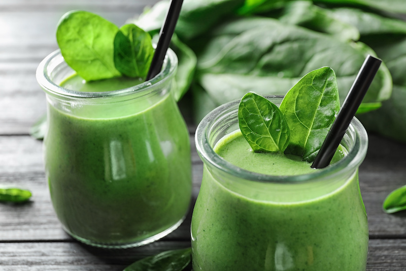Jars of healthy green smoothie with fresh spinach on grey wooden table, closeup
